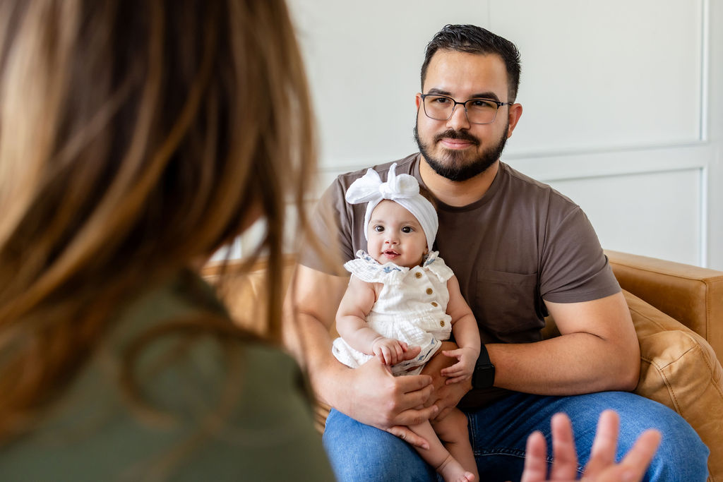 A father holding an infant while talking with a clinician