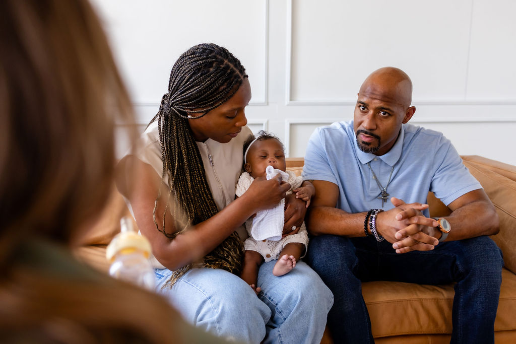 A caregiver attending to her infant while talking with a clinician beside the other parent