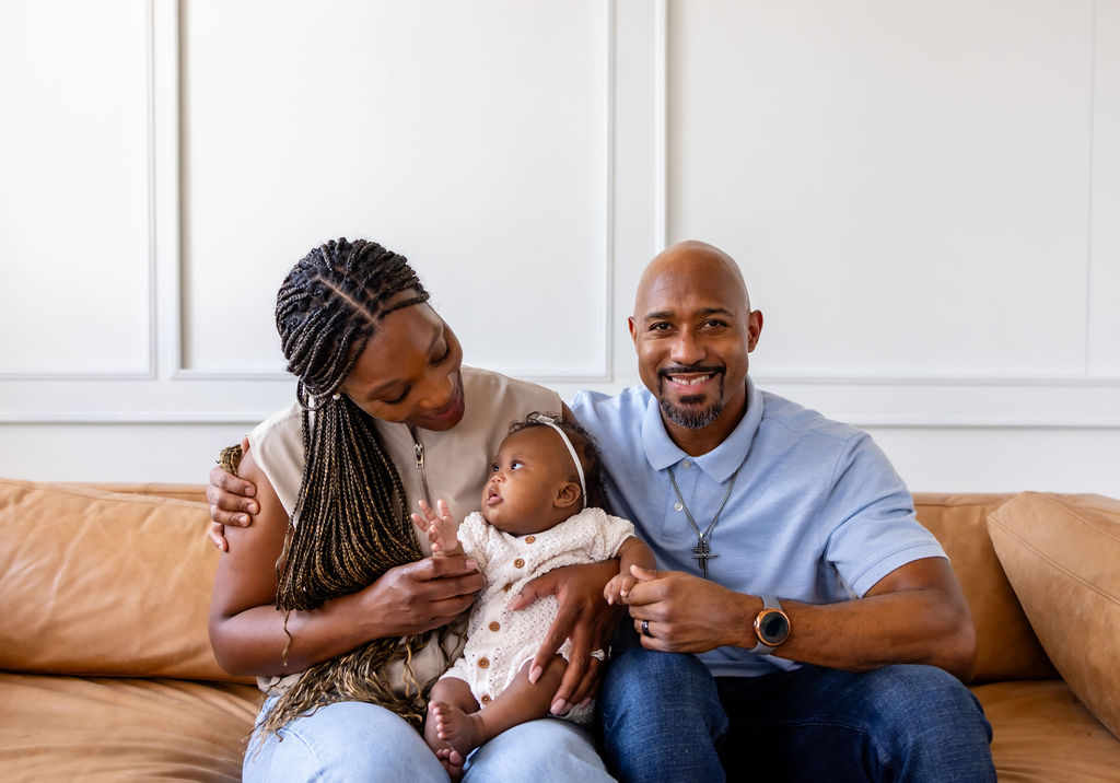 Parents smiling with their infant while seated together on a sofa