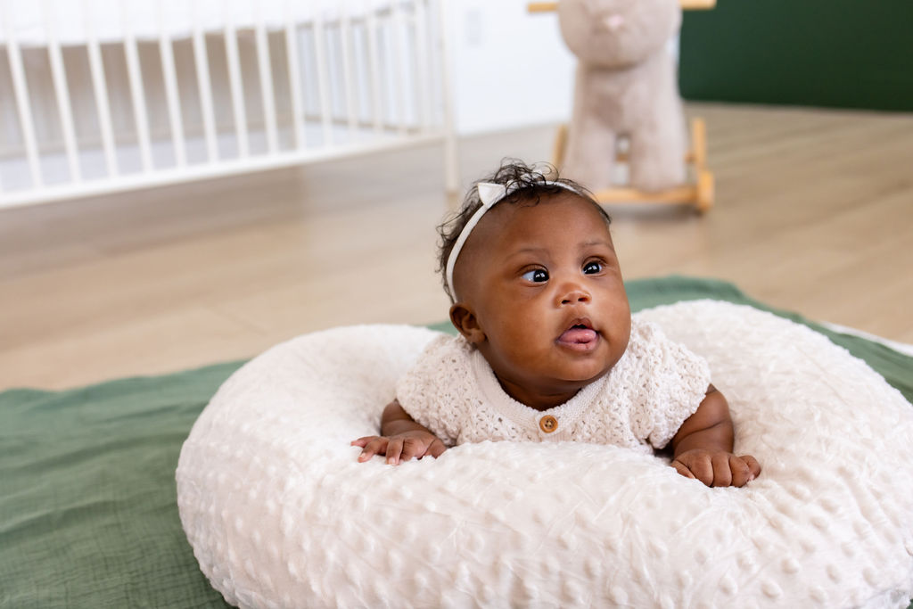 An awake infant looking up during tummy time on a white cushion