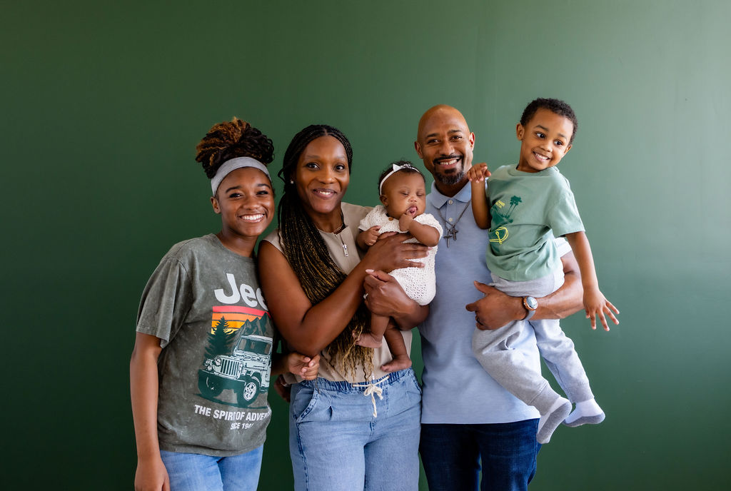 A family with parents, an infant, and older children posing against a green background