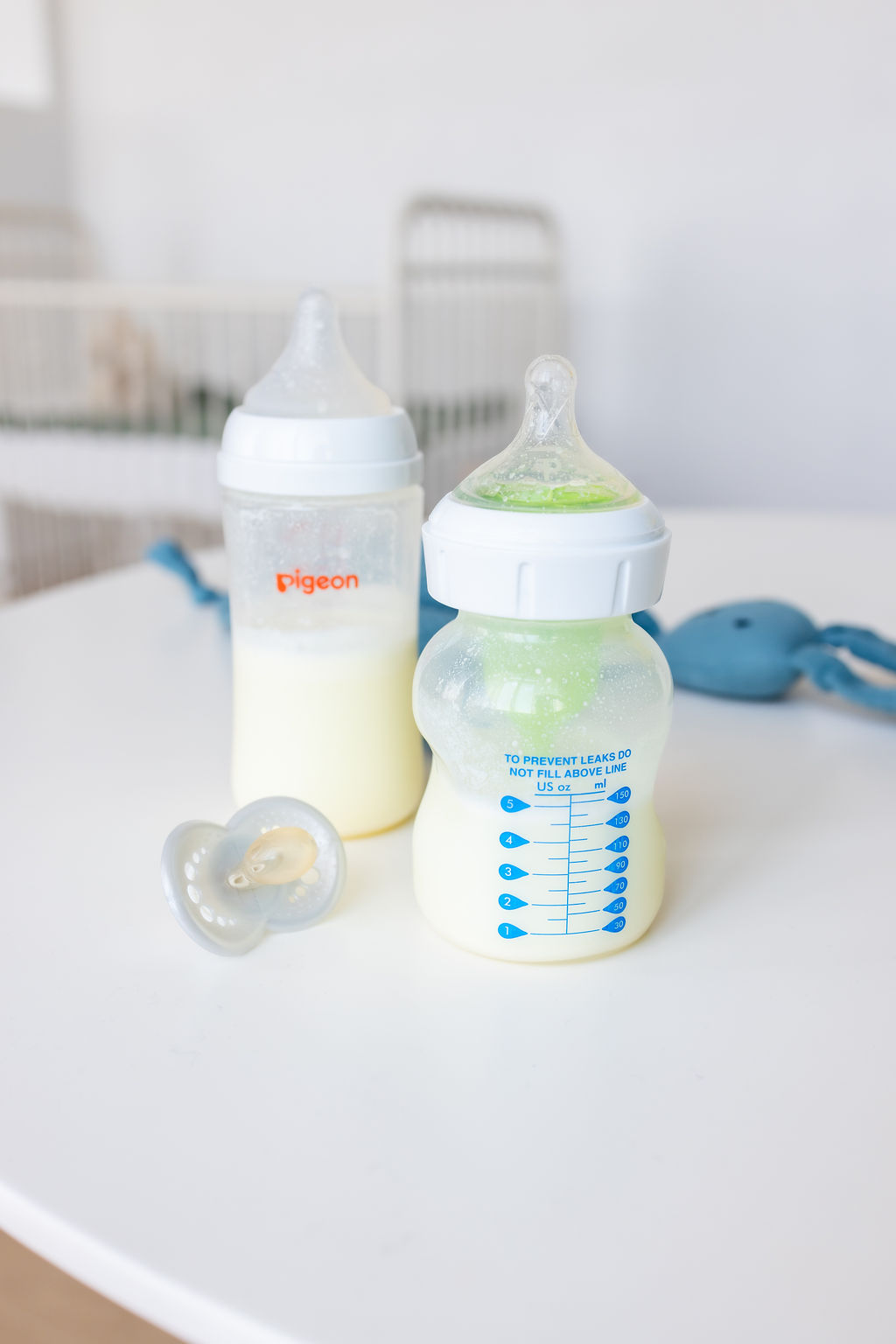 Two baby bottles containing milk on a white surface beside bottle accessories