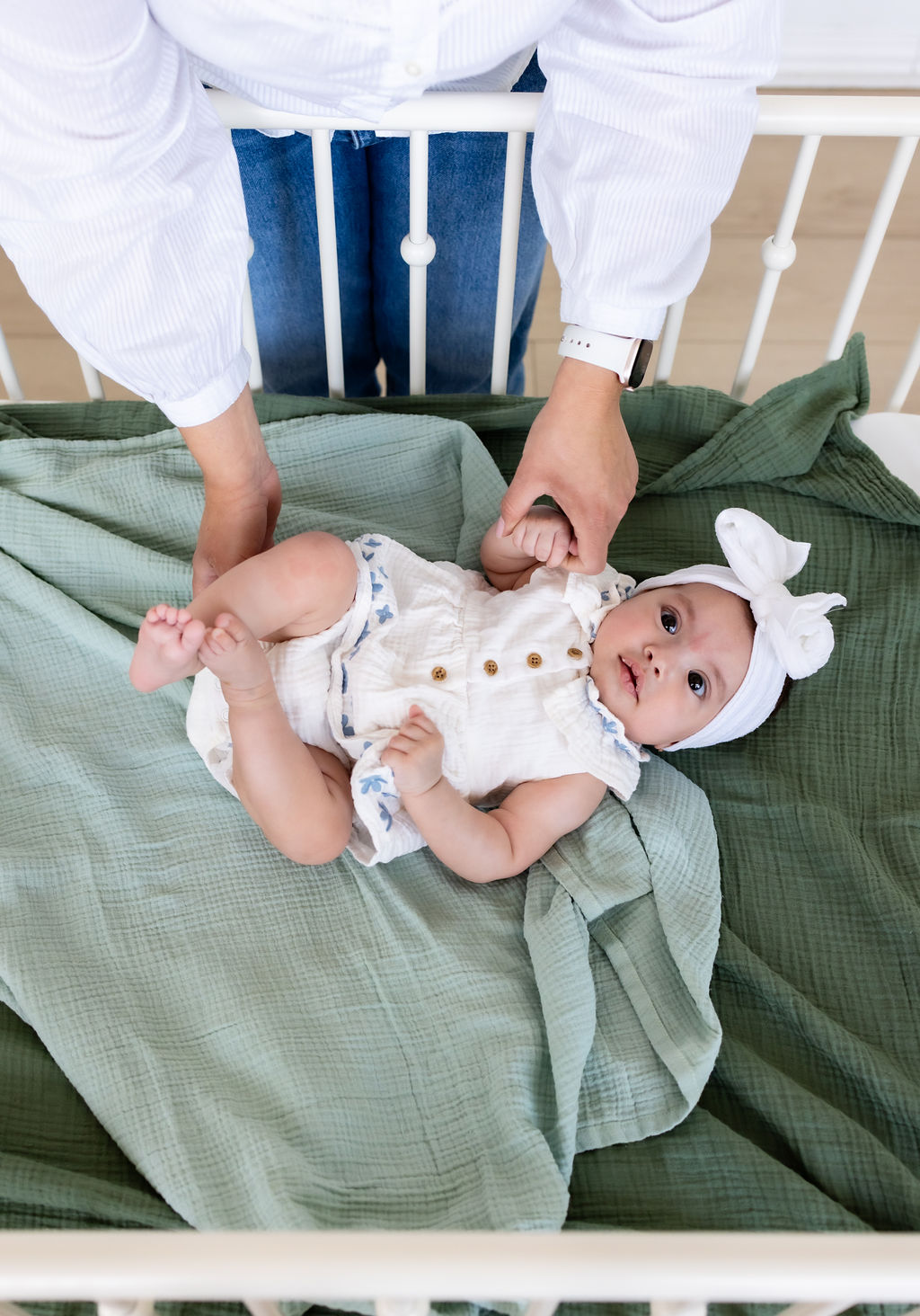 Caregiver gently touching the legs of an awake infant lying on a green blanket