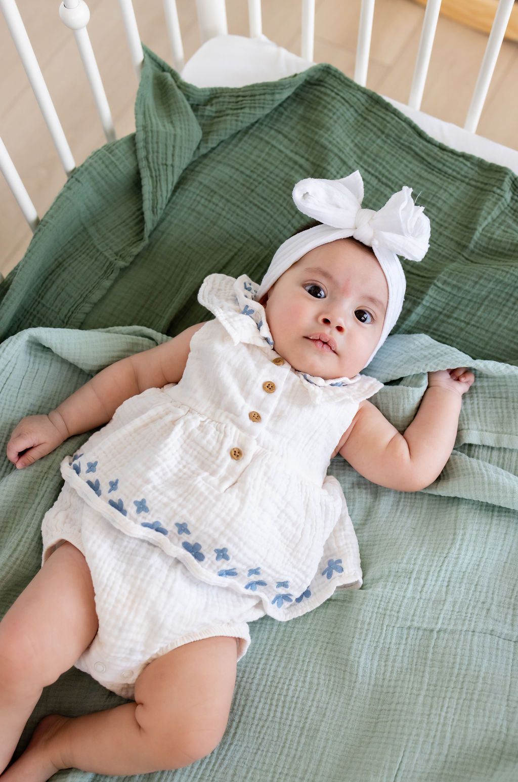 An awake infant lying on a green blanket in a crib