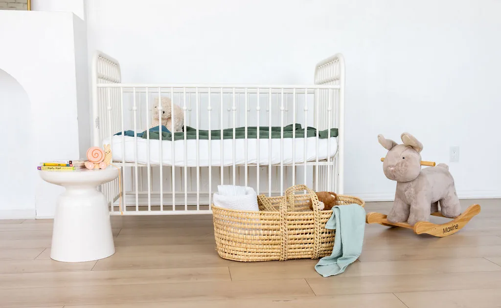 White crib with baskets, toys, and a wooden rocking animal