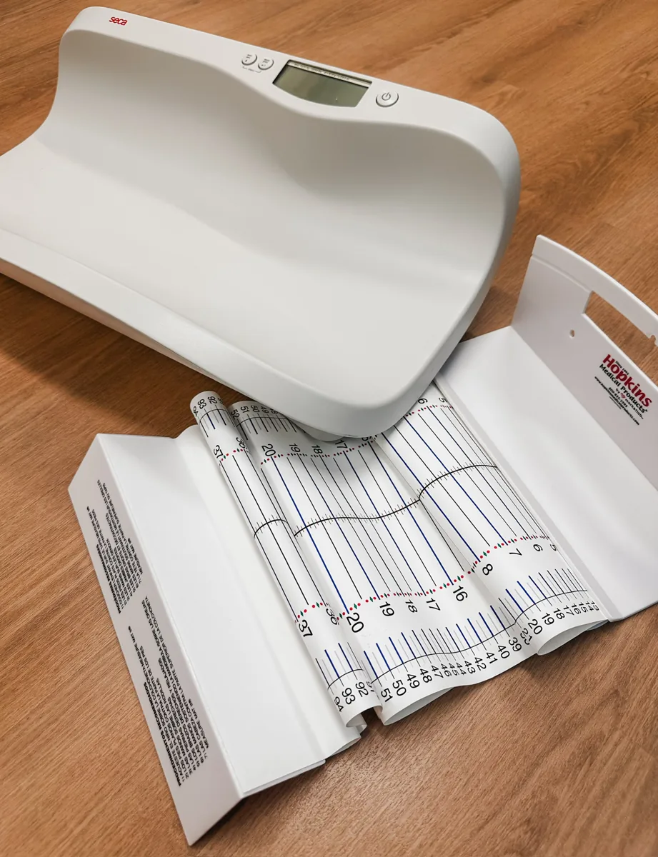 Infant scale beside a printed growth chart on a wood surface